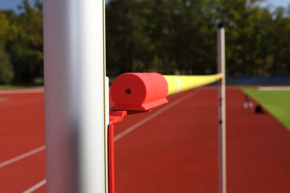 Yellow fibreglass high jump crossbar with red plastic end seated on a metal upright over a red running track.